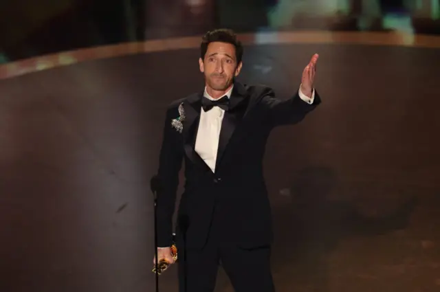 Adrien Brody with his hand stretched out to the crowd holding his Oscar in his other hand