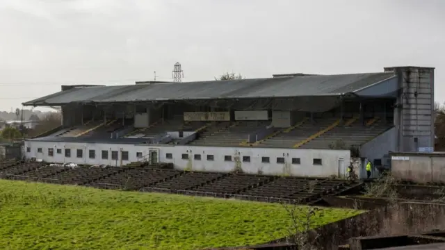 A dilapidated Casement Park sits empty and in front of an overgrown pitch.