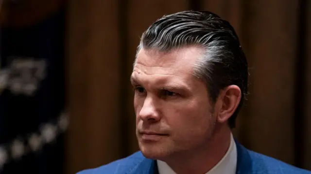 Pete Hegseth on right side of image, gazing off-camera to the left. Visible, are the shoulders of his light blue blazer, and the top part of his white shirt collar.