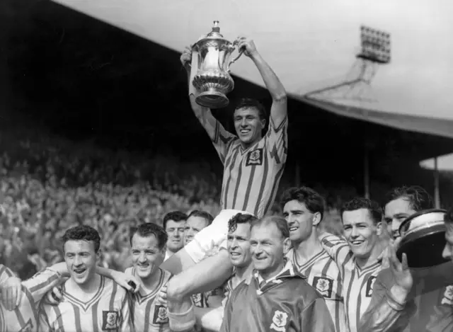 Aston Villa captain J Dixon lifts the FA Cup trophy as he is carried on the shoulders of his team-mates after their 2-1 win over Manchester United in the FA Cup final in 1957.