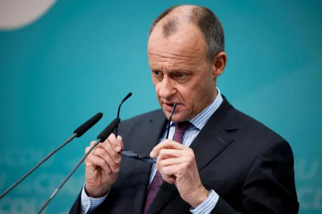 Friedrich Merz, chancellor-in-waiting and leader of Christian Democratic Union party, holds his eyeglasses as he addresses the media following the federal state election of Hamburg