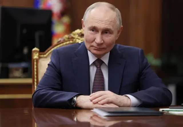 Vladimir Putin looks on, while he sits at a desk