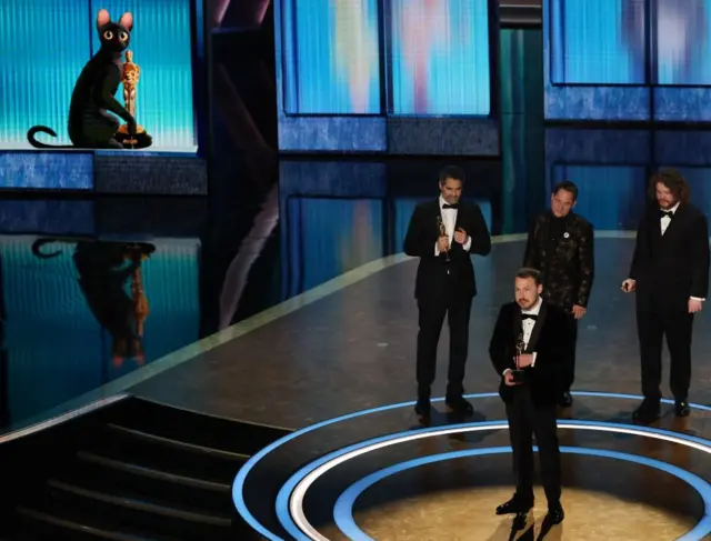 Gints Zilbalodis holding the Oscar with Matiss Kaza, Ron Dyens and Gregory Zalcman stood behind him on the Oscars stage