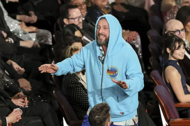 Adam Sandler in a blue hoody standing in the Oscars audience