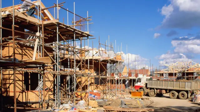 A housing development is under construction. A lorry is in the middle of the building site and the house are surrounded in scaffolding.