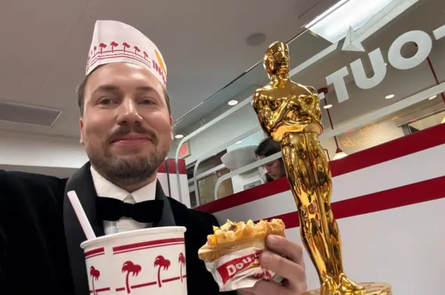 Gints Zilbalodis poses with a burger and a drink alongside his Oscar at In-N-Out Burger