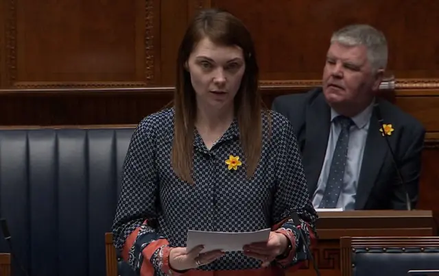 Jemma Dolan has long brown hair. She is wearing a dotted black and white blouse with red and navy hoops around the sleeves.