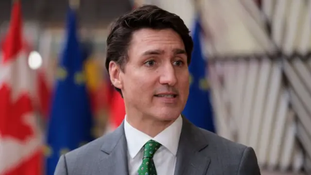 Canada's Prime Minister Justin Trudeau, in grey suit and green tie, at the EU Council's headquarters. In the background are Canada's and the EU's flags