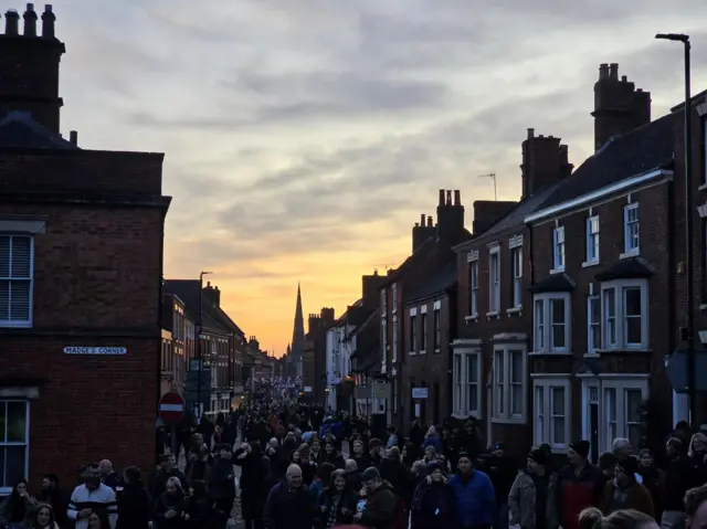 Sun setting in the sky over Ashbourne with crowds of people taking part in the game