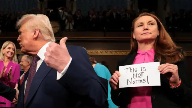 U.S. President Donald Trump arrives for his speech to a joint session of Congress as Rep. Melanie Stansbury (D-NM) holds a sign reading "This is not normal" at the U.S. Capitol on