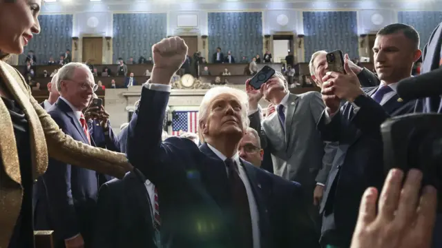 Donald Trump holds his fist in the air, surrounded by people taking photos and congratulating him