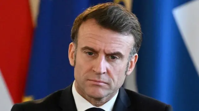 A file photo of Macron. He is seated in front of country flags and wearing a dark suit