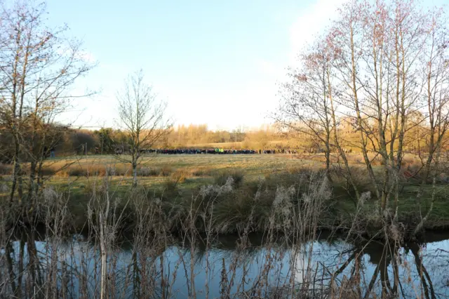 A brook at the front of the photo and on the other side, in the distance, a crowd can be seen - also known as the hug