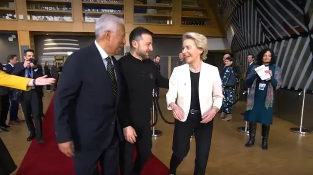 Antonio Costa (L), Volodymyr Zelensky (C) and Ursula von der Leyen (R) walk together as they chat and smile along a red carpet inside the European Parliament building in Brussels