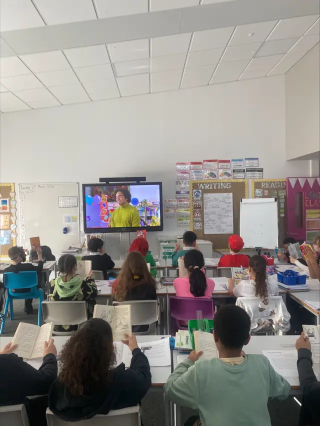 A group of children sat in a classroom facing a screen.