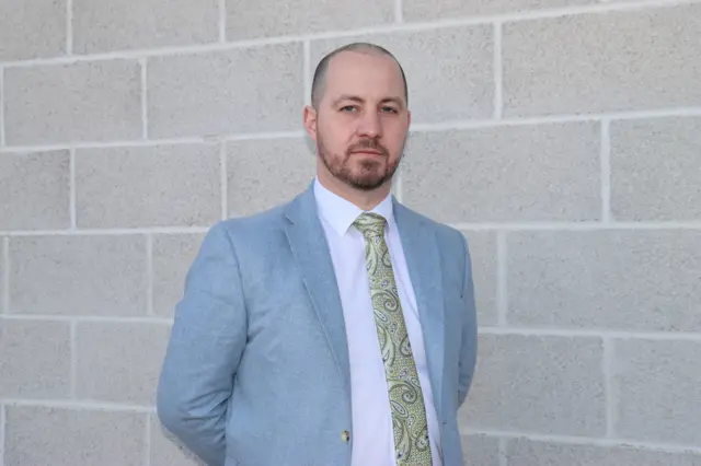 Nick Gardner wearing a blue suit jacket and a paisley gold tie