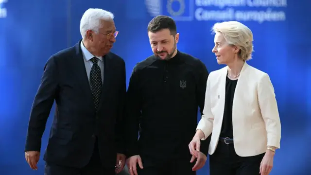 Antonio Costa (R), Volodymyr Zelensky (C) and Ursula von der Leyen (R) walking together inside the European Parliament building in Brussels, a blue wall with the European Council logo on a blue wall blurred in the background