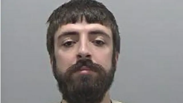 Mugshot of Clifford, he is looking at the camera and has a thick beard and moustache