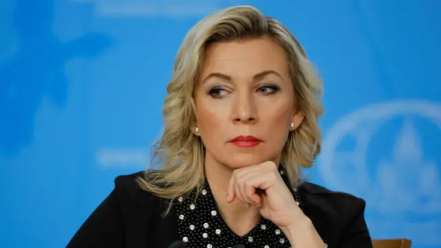 Russian Foreign Ministry spokeswoman Maria Zakharova wears a black shirt in front of a blue backdrop.