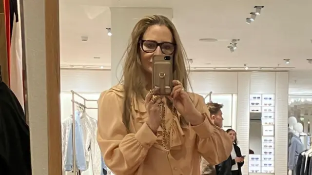 Anna takes a photo of herself in a mirror in a clothing shop