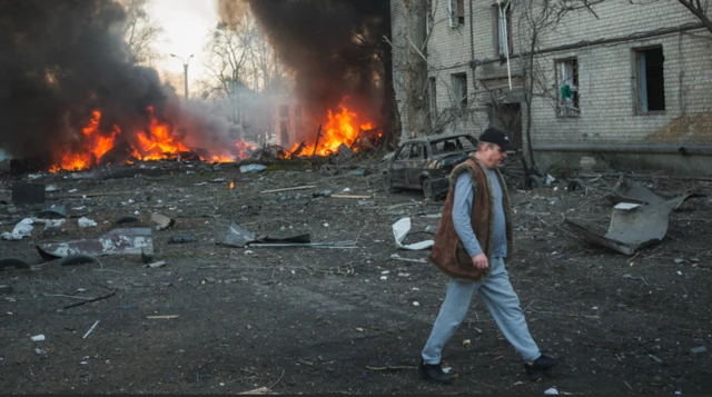 Emergency teams and civilians are at the scene where a Russian Iskander missile hit a civilian infrastructure facility, causing an explosion and therefore fire and damage in ten garages and five cars in Kharkiv. A man walks in the foreground while the fires rage behind him some distances away