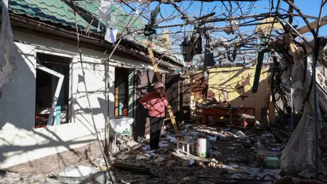 A woman stands near a house in Odesa which has been destroyed by a strike - there is rubble everywhere