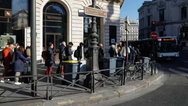 People queue around a corner on the street in Paris as they wait for buses