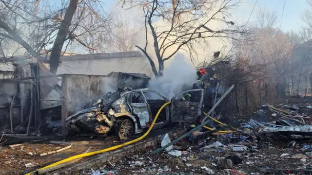 Firefighters work at the site of a missile strike in Kharkiv - a battered car can be seen next to a building that has also been hit