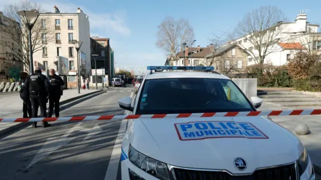 Red and white tape marks off a street, with a police car parked in the road and officers standing in the background