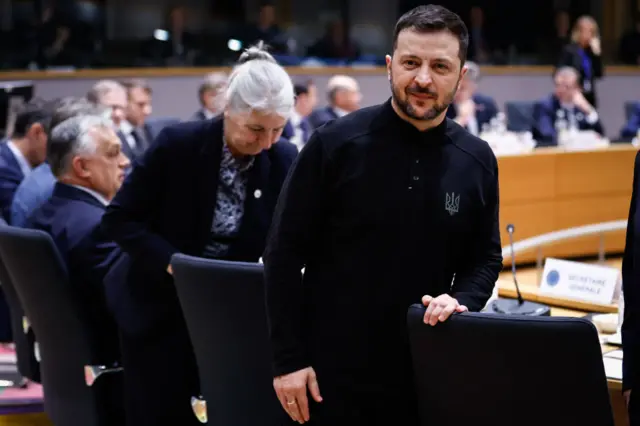 Ukrainian President Volodymyr Zelenksy wearing black, standing up from seat in parliamentary chambers.