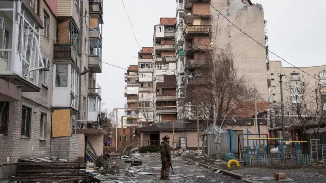 A Ukrainian serviceman stands near residential buildings damaged by Russian military strikes in Pokrovsk