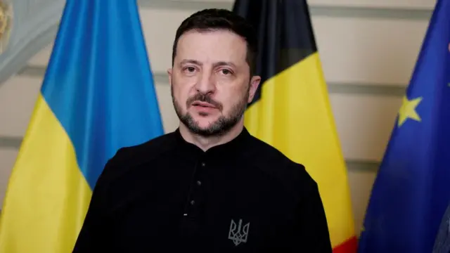 Ukrainian President Volodymyr Zelenksy stood in front of three flags, wearing a black shirt.