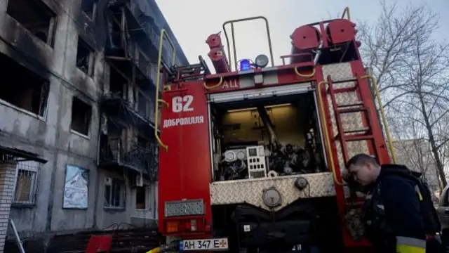 A firefighter leans on a fire truck near a damaged residential building following a strike in Dobropillia