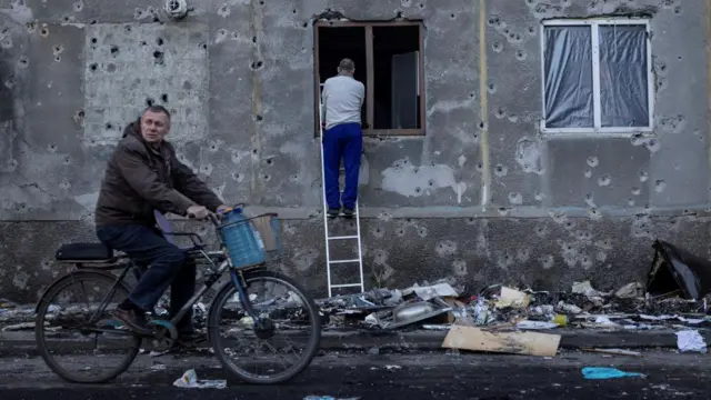 A resident covers a broken window in his apartment damaged by a Russian missile strike as traces of shrapnel are seen on the wall