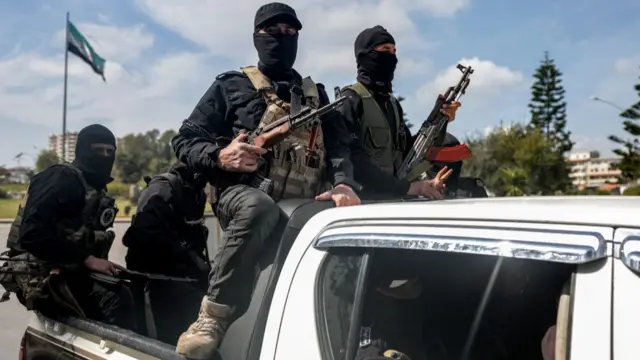 Masked men holding guns ride on the back of a truck