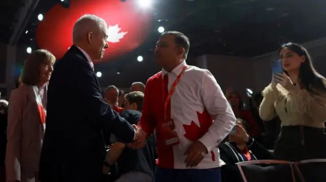 Frank Baylis in dark suit shakes hands with man in Canadian flag shirt