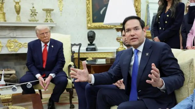 Trump sit son a gold armchair at the background on a photo. In the foreground Rubio sits on a sofa speaking with both his arms spread out in front of him