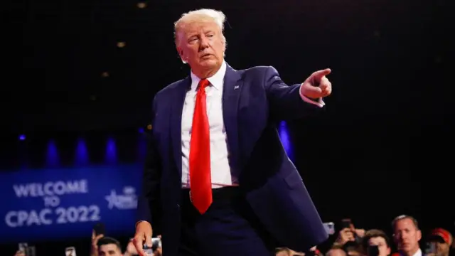 Trump standing in front of a crowd in a suit pointing