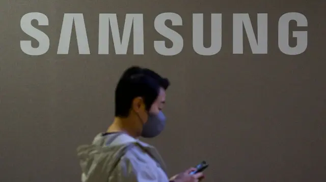 A man looking at his phone as he walks past a Samsung sign