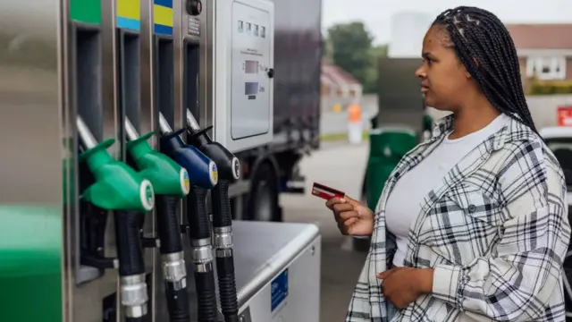 A woman stands at a petrol pump to refill her car.
