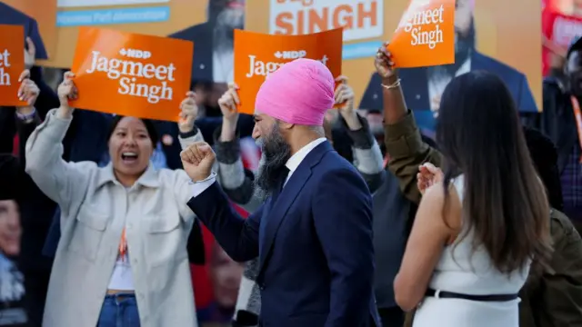 Singh walking along with a fist raised, as a crowd stands behind him smiling and holding signs with his name on