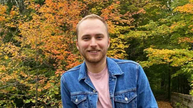 A picture of Thomas Stenlake standing in front of trees in autumn