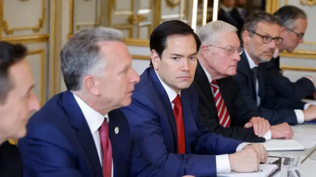 US Special Envoy Steve Witkoff (2L), US Secretary of State Marco Rubio (C)  and Special Envoy Keith Kellogg (2R) sit at a table wearing black suits and red ties, surrounded by other officials.