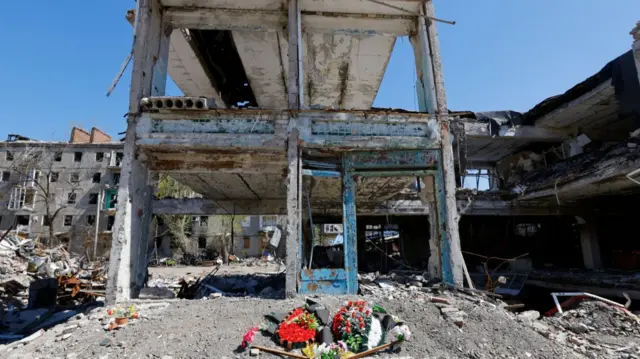 Flower tributes lay in front of bombed out structure in Donetsk, Ukraine on  sunny day, blue skies with no cloud