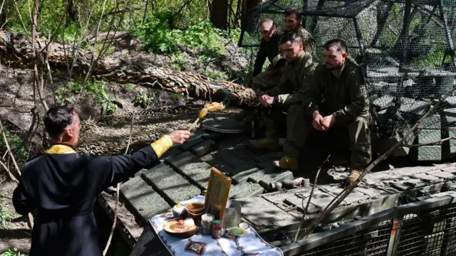 A military chaplain sprays holy water on Ukrainian soldiers on the front lines.