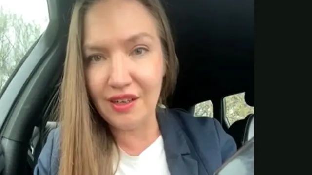Victoria Vdovychenko speaks to BBC News Channel. She wears a blue blazer and is sitting behind the wheel of her car.