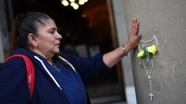 A woman holds her hand to a wall.