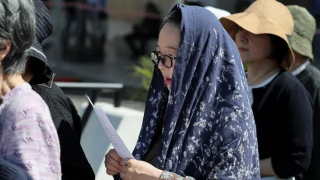 A woman with a scarf covering her head is reading something from a piece of paper