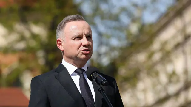 Polish president Duda delivers speech outdoors while standing in a black suit with matching tie and white shirt