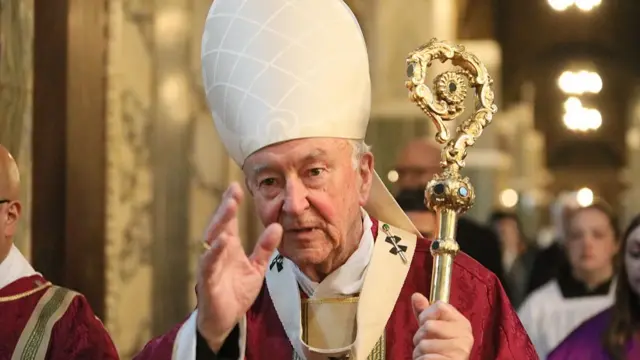 A man in a clerical outfit gestures while holding a golden staff